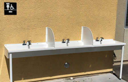 Public outdoor trough sink with 3 faucets and splash dividers.